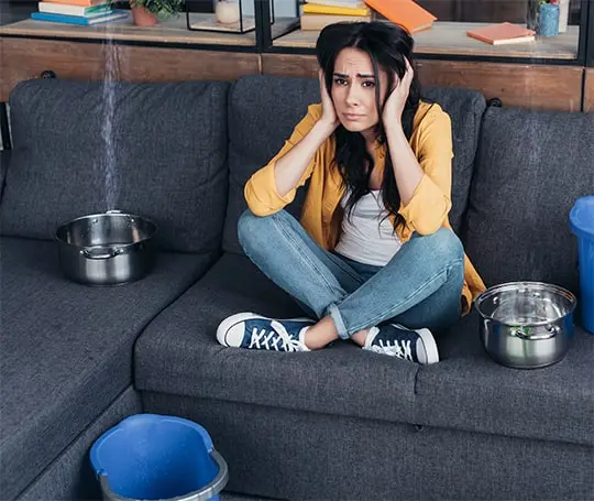 Upset woman in her home surrounded by buckets catching dripping water from leaking roof 