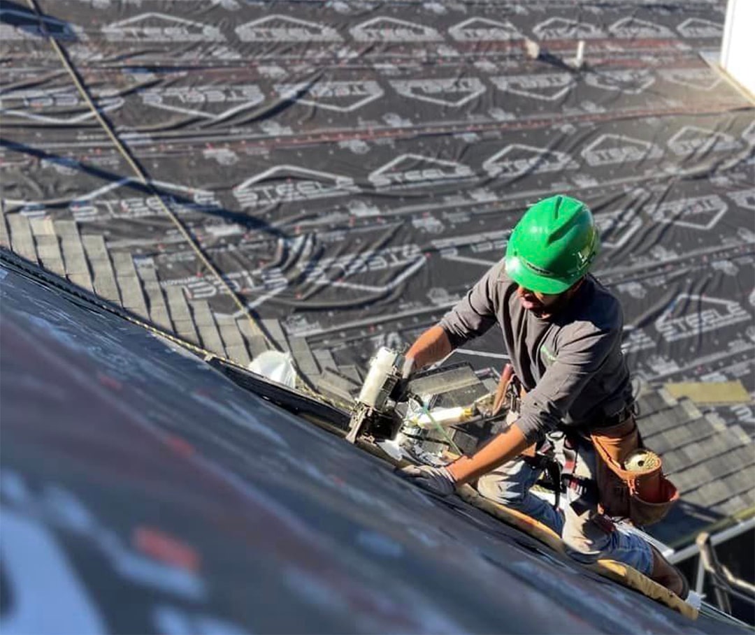 A worker with a green cap is working to repair the roof.