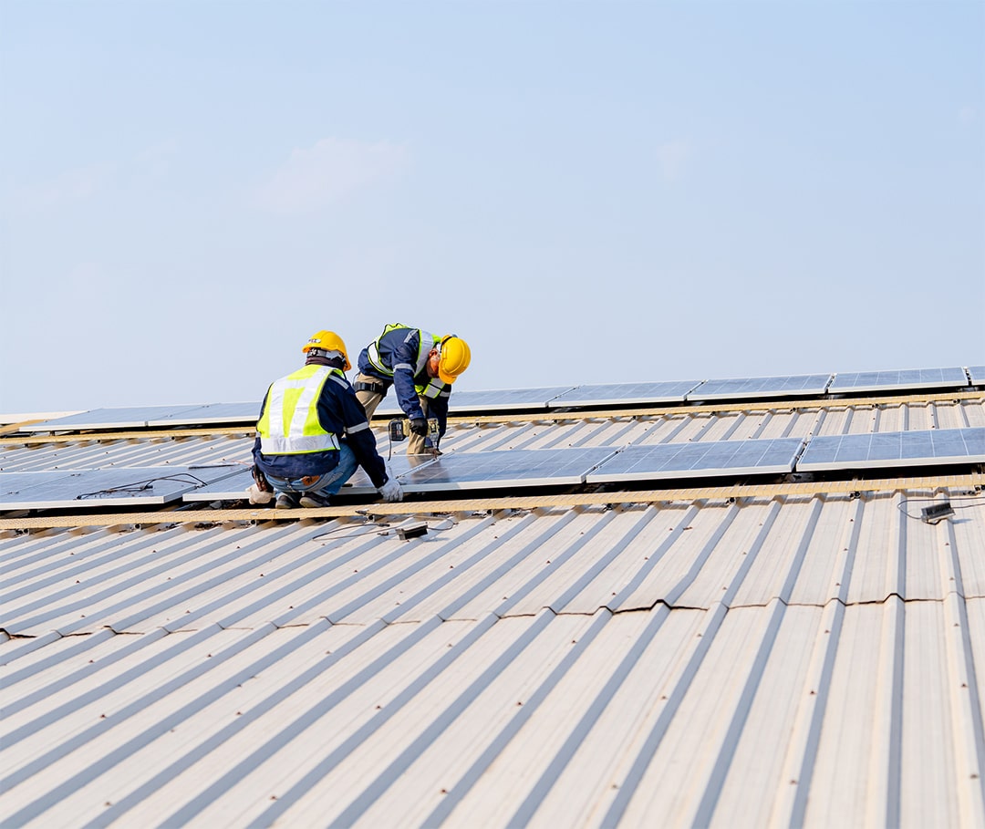 Two repairmen are working on a repair of a gray commercial roof.