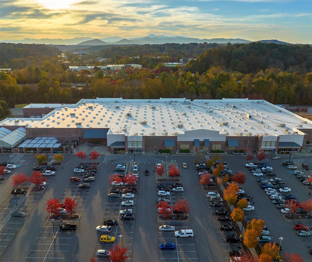 A bird's-eye view of the office building and the parking lot with cars in front of it. In the foreground is a large roof because of the importance of solving the problem of roof leaks.