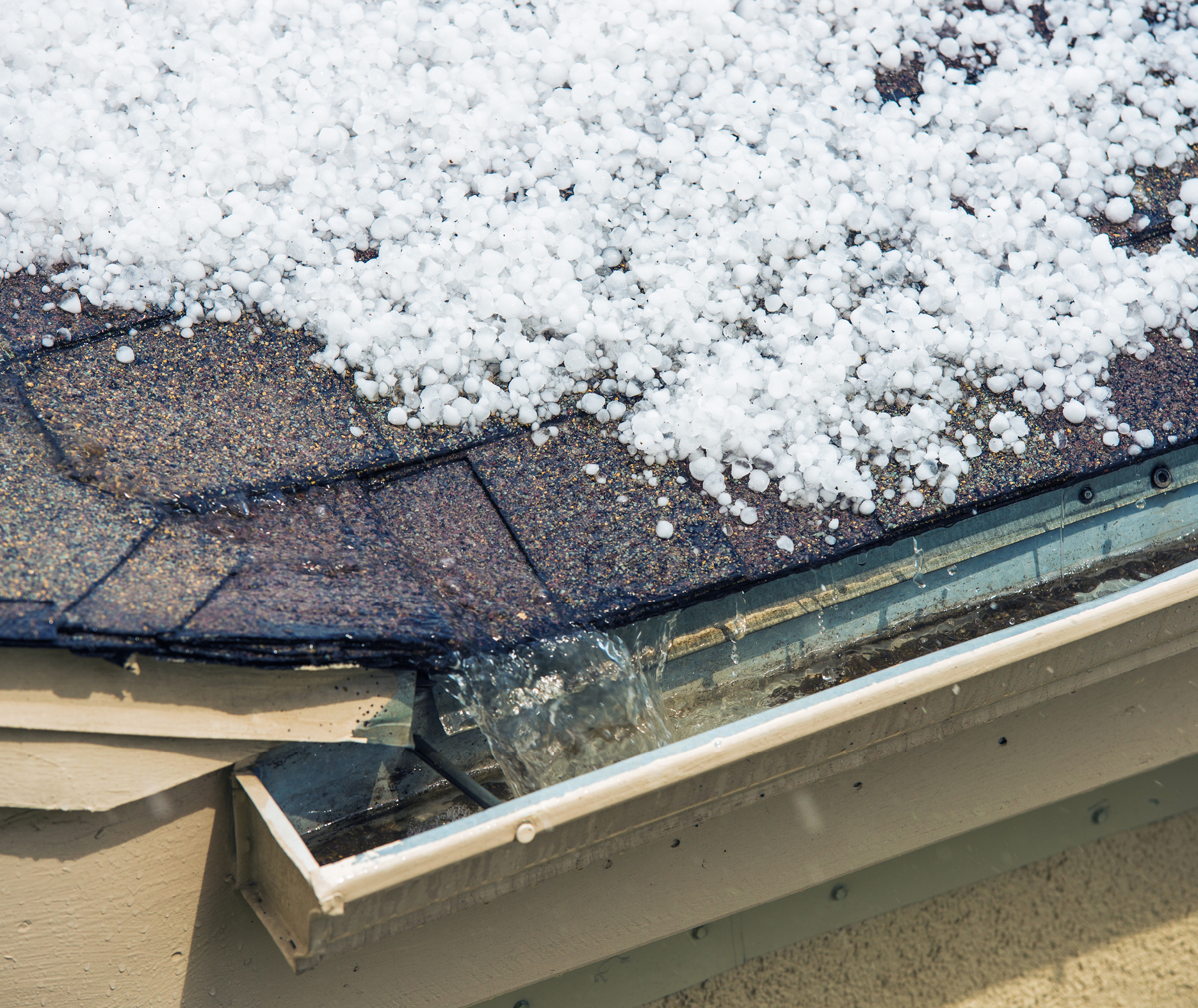 Hail accumulated on asphalt shingle roof edge draining into gutter
