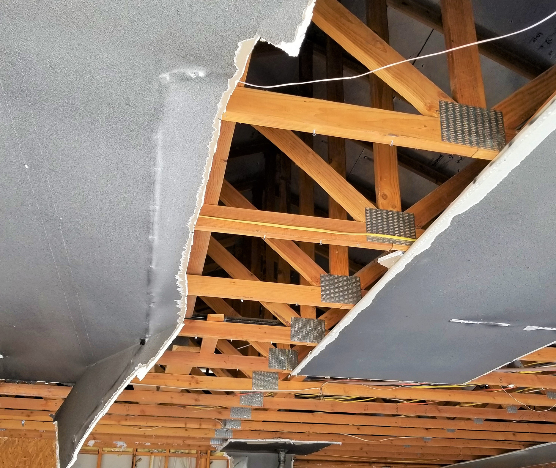 Collapsed drywall ceiling exposing wooden roof trusses with metal gusset plates and electrical wiring